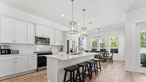 A modern kitchen with white cabinetry, stainless steel appliances, and a central island with bar stools. - Vacation Station with Private Pool and Low-Speed Vehicle (Miramar Beach)