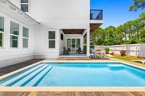 Et moderne hus med en swimmingpool, en overdækket terrasse og udsigt over det grønne landskab.