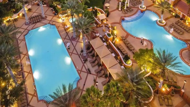 A hotel courtyard with two swimming pools, palm trees, and outdoor seating areas. - Resort near airport, convention center & casinos. (Las Vegas)