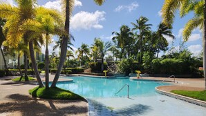 Piscina rodeada por palmeiras e um céu azul límpido.