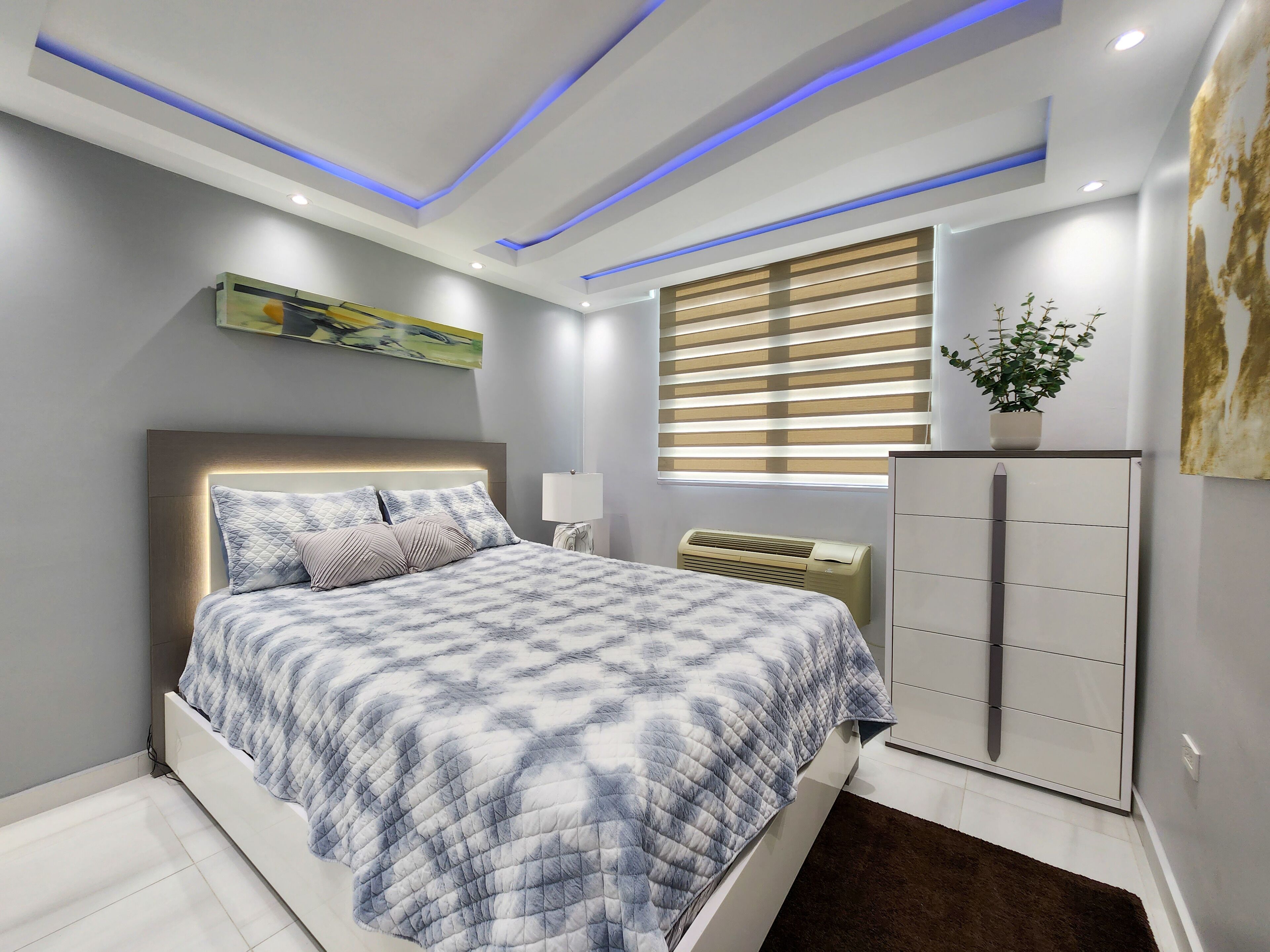 A modern bedroom with a bed, bedside lamp, air conditioner, and a cabinet.