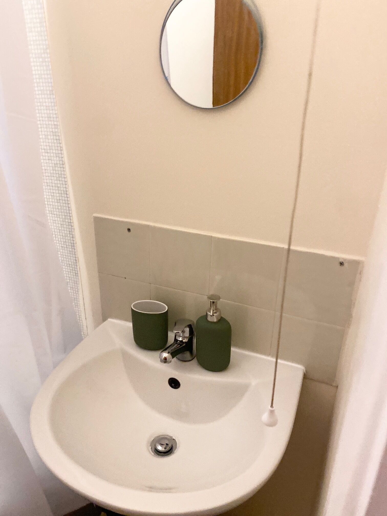 A bathroom with a white sink, green soap dispenser, and a cup.