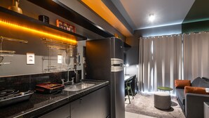 Una cocina moderna con electrodomésticos de acero inoxidable, horno empotrado y encimera de granito. Hay una zona de comedor con sofá y una mesita redonda.