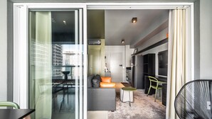 Un apartamento moderno con puerta de vidrio corrediza que da a un balcón, una zona de cocina y una sala de estar con sofá y sillones.