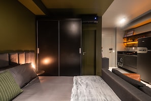Quarto moderno com uma cama grande, área de estar separada e uma kitchenette.