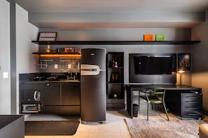 Uma cozinha compacta com eletrodomésticos embutidos, uma área de refeições com uma cadeira e uma TV fixada na parede.