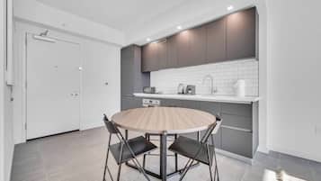 A modern kitchen with a round wooden table and black chairs, a white door, and grey cabinets.