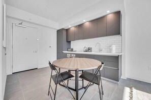 Eine moderne Küche mit einem runden Holztisch, schwarzen Stühlen, einer weißen Tür und grauen Schränken.