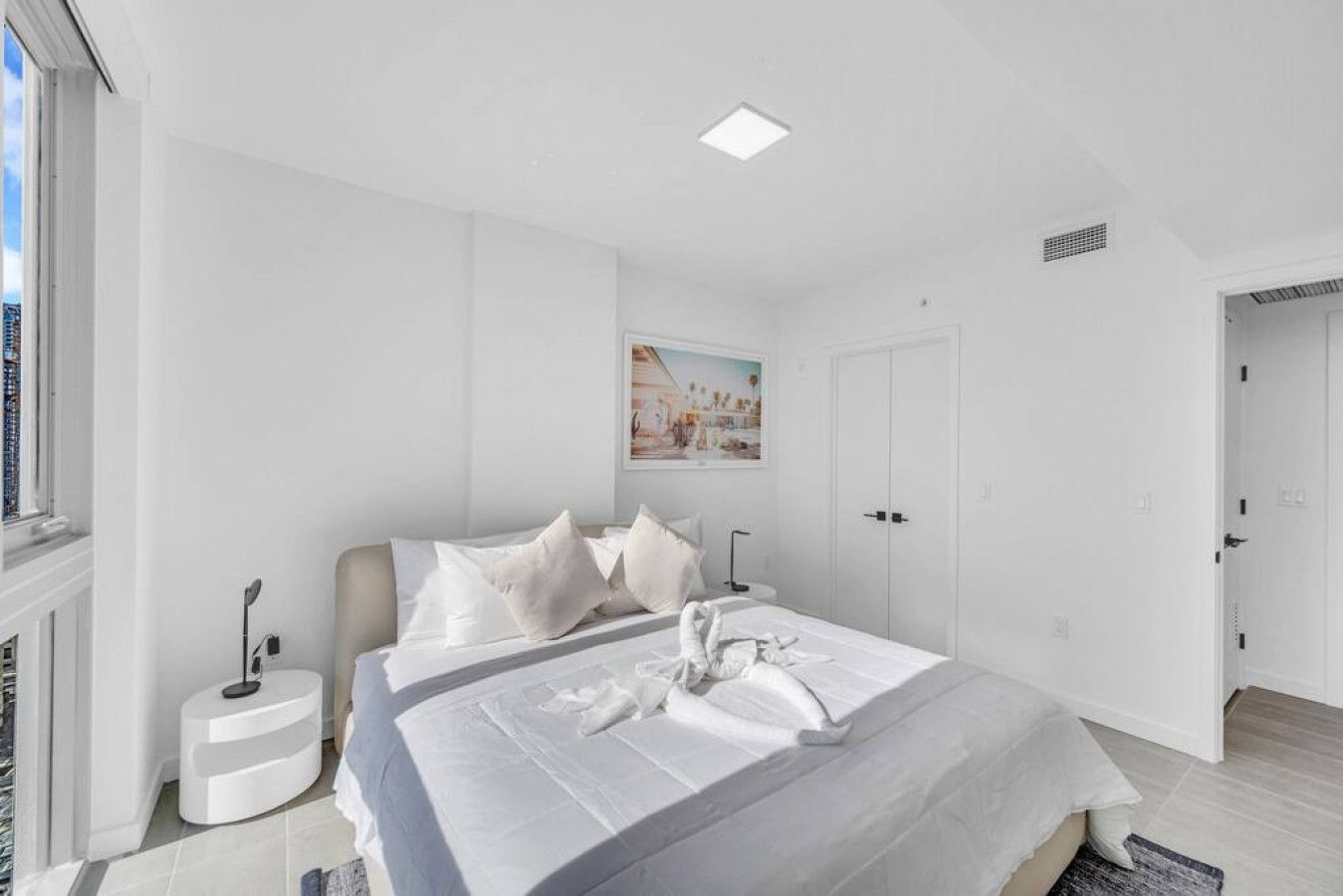 A modern bedroom with a large bed, a bedside table, a wall-mounted light, and a painting.