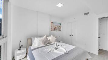 A modern bedroom with a large bed, a bedside table, a wall-mounted light, and a painting.