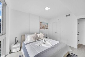 A modern bedroom with a large bed, a bedside table, a wall-mounted light, and a painting.