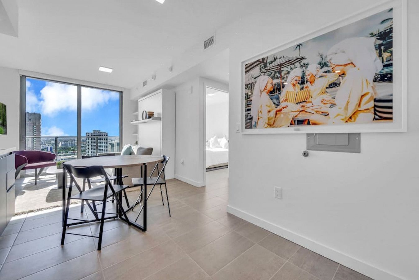 A modern apartment with a dining area, a large window with a city view, and a framed artwork on the wall.