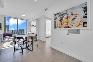 Eine moderne Wohnung mit Essbereich, einem großen Fenster und Blick auf die Stadt sowie einem gerahmten Kunstwerk an der Wand.
