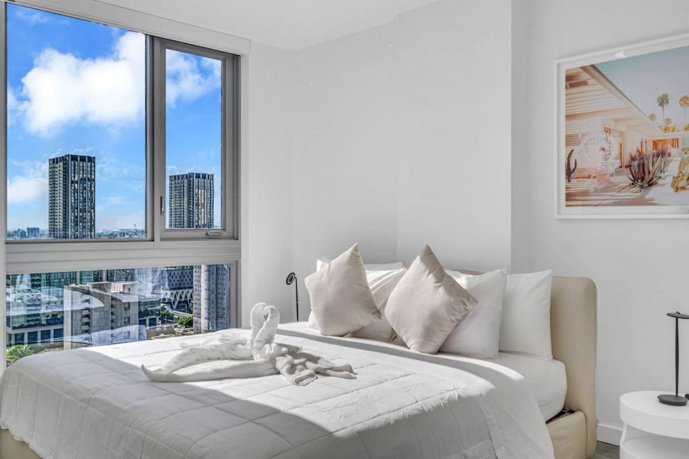 Una habitación de hotel moderna con una cama grande, ropa de cama blanca y vistas a la ciudad a través de amplios ventanales.