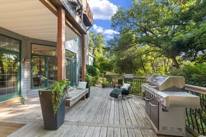 Una terraza de madera con mobiliario exterior, una parrilla y plantas en macetas.