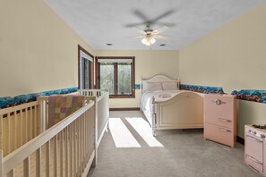 Ein Schlafzimmer mit einem Bett, einem Babybett, einer Kommode und einem Deckenventilator.