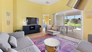 A living room with a sofa, a TV, a cabinet, and a view of a pool through glass doors. - Private Pool, Gated Golf Community (Kissimmee)