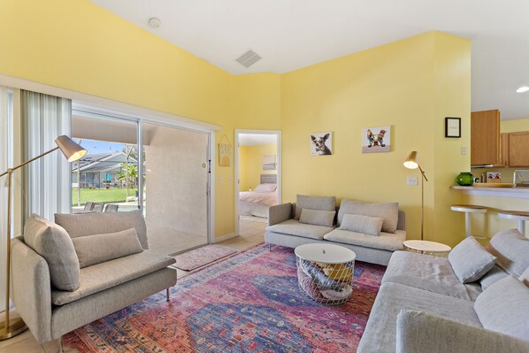 A living room with a sofa, a coffee table, and a rug. There is a sliding glass door leading to a balcony.