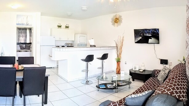 A modern living room with a sofa, a dining area with chairs, a kitchen with white cabinets, and a small island. - Cozy, Cole Bay, one bedroom with security and free parking (Cole Bay)