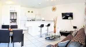 A modern living room with a sofa, a dining area with chairs, a kitchen with white cabinets, and a small island.