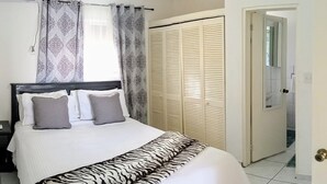 A neatly made bed with a patterned bedspread, a bedside table with a lamp, and a wardrobe with louvered doors. - Cozy, Cole Bay, one bedroom with security and free parking (Cole Bay)