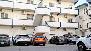 A parking lot with several cars parked in front of a multi-story building with balconies and air conditioning units. - Cozy, Cole Bay, one bedroom with security and free parking (Cole Bay)