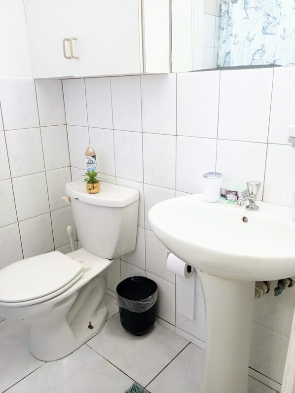 Une petite salle de bain propre, avec des accessoires blancs, des toilettes, un lavabo et une poubelle.