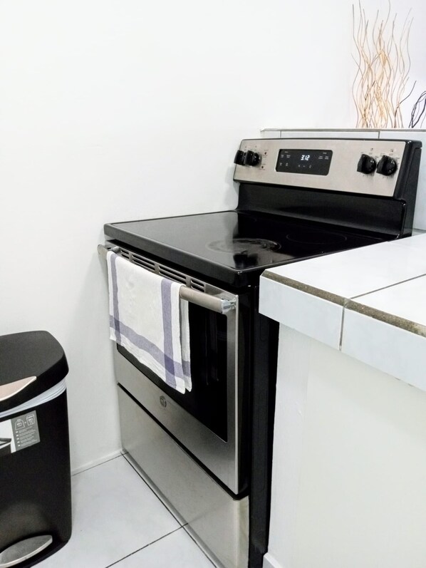A kitchen with a black and stainless steel stove, a trash bin, and white tiled walls.
