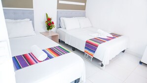 Una habitación de hotel con dos camas individuales, una mesita de noche con un jarrón de flores y una manta tejida de colores sobre cada cama.