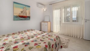 A bedroom with a bed, a painting of a sailboat, a small cabinet, and a window with curtains. - 2 bedroom cozy apartment in Crikvenica (Crikvenica)
