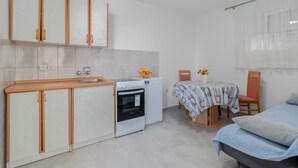 A compact kitchen with a sink, stove, and refrigerator, a small dining table with chairs, and a bed with a blue blanket. - 2 bedroom cozy apartment in Crikvenica (Crikvenica)