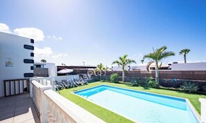 Ein Swimmingpool mit weißer Liegefläche, einer Rasenfläche und Palmen.