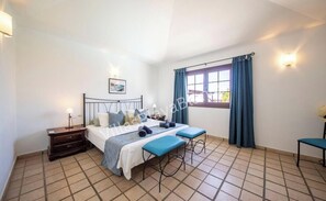 Ein Schlafzimmer mit Bett, Nachttisch, Bank, Fenster mit Vorhängen und einem Bild an der Wand.