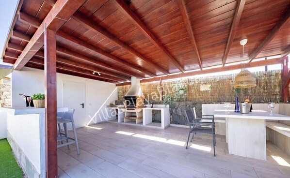 Eine Terrasse im Freien mit Holzboden, einer Steinsäule und einer Sitzecke mit Tisch und Stühlen.
