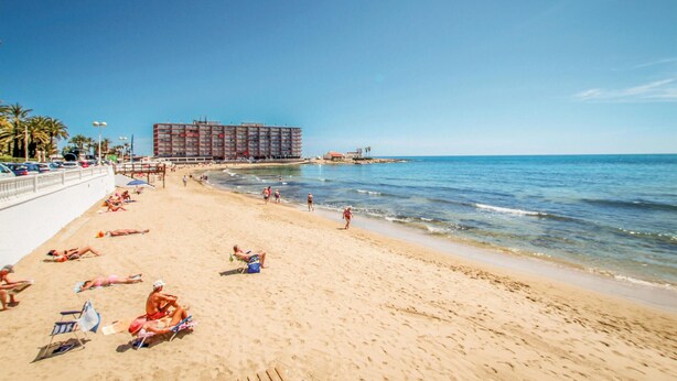 Een strand met een groot hotel op de achtergrond, zandstrand en helderblauwe lucht.