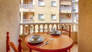 Een balkon met een houten tafel gedekt voor twee personen, een stoel en uitzicht op een appartementencomplex.