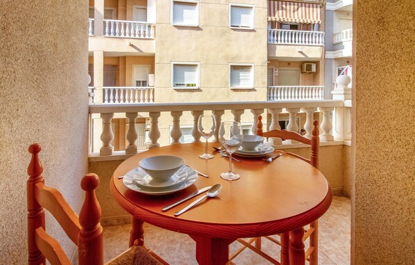 A balcony with a wooden table set for two, a chair, and a view of an apartment building. - Stunning apartment in Torrevieja (Torrevieja)