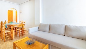 Een woonkamer met een bank, een houten eettafel, stoelen en een salontafel.