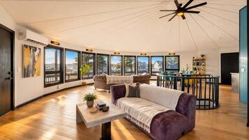 A spacious living area with a large window, a ceiling fan, and a dining area.