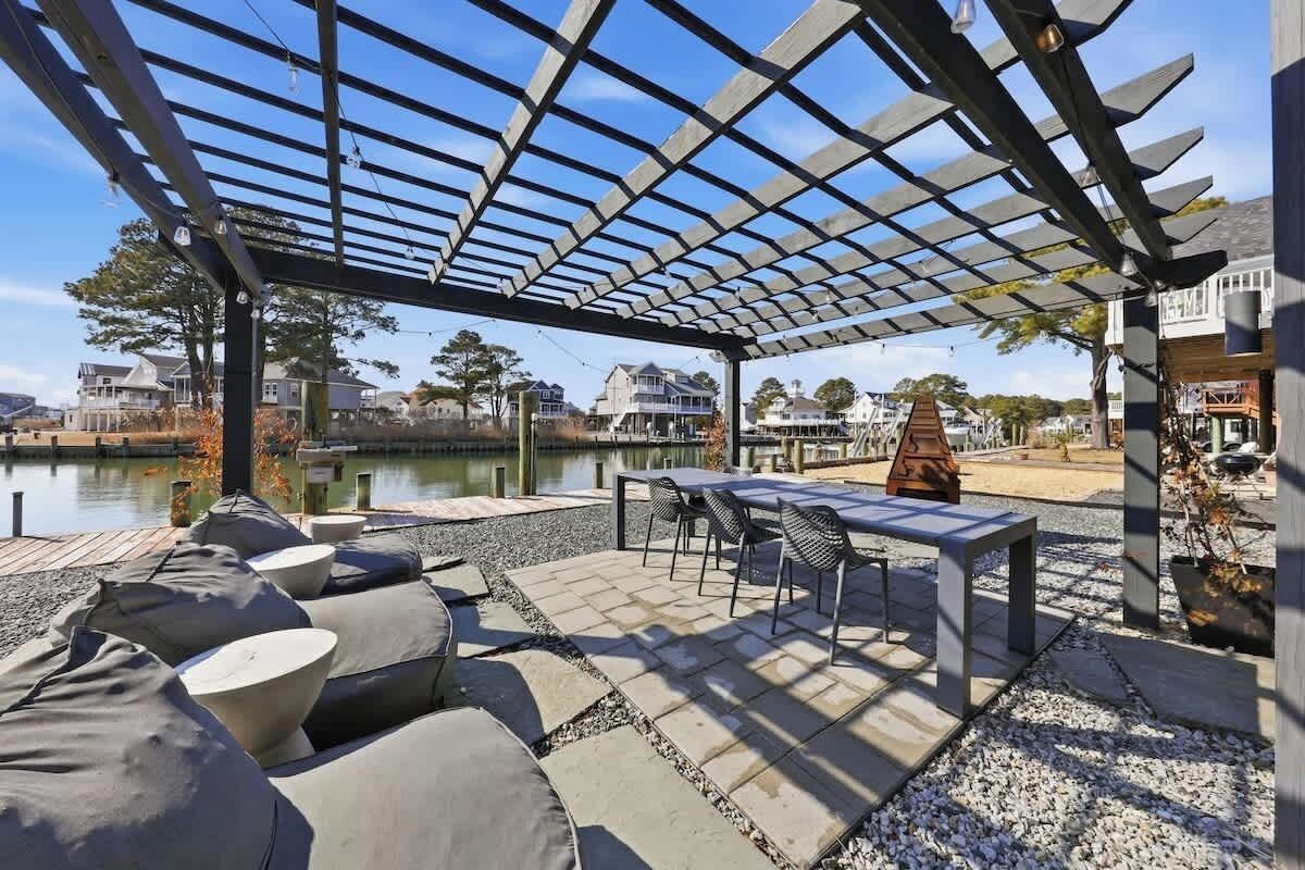 An outdoor patio with a pergola, seating, and a view of a body of water and houses.