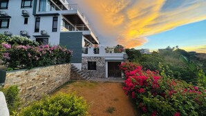 A modern multi-story building with balconies, a stone wall, and a garden with pink flowers. - Picturesque private villa with infinity pool (Puerto Galera)
