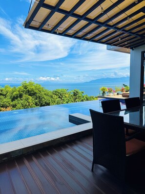 Ein Infinity-Pool auf dem Dach mit Blick auf das Meer und die Berge, eine überdachte Lounge und Kübelpflanzen.