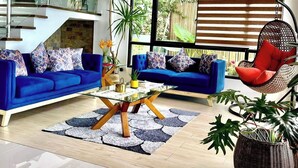 A spacious living room with a blue sofa set, a glass coffee table, and a hanging chair. There is a staircase with glass railings leading to an upper level. - Picturesque private villa with infinity pool (Puerto Galera)