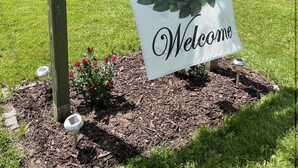 A wooden signpost with a 'Welcome' sign and a wreath, set in a landscaped area with mulch and flowers. - Winding River - Panoramic view of river valley, under 10 minutes to Dreams Park (Cooperstown)