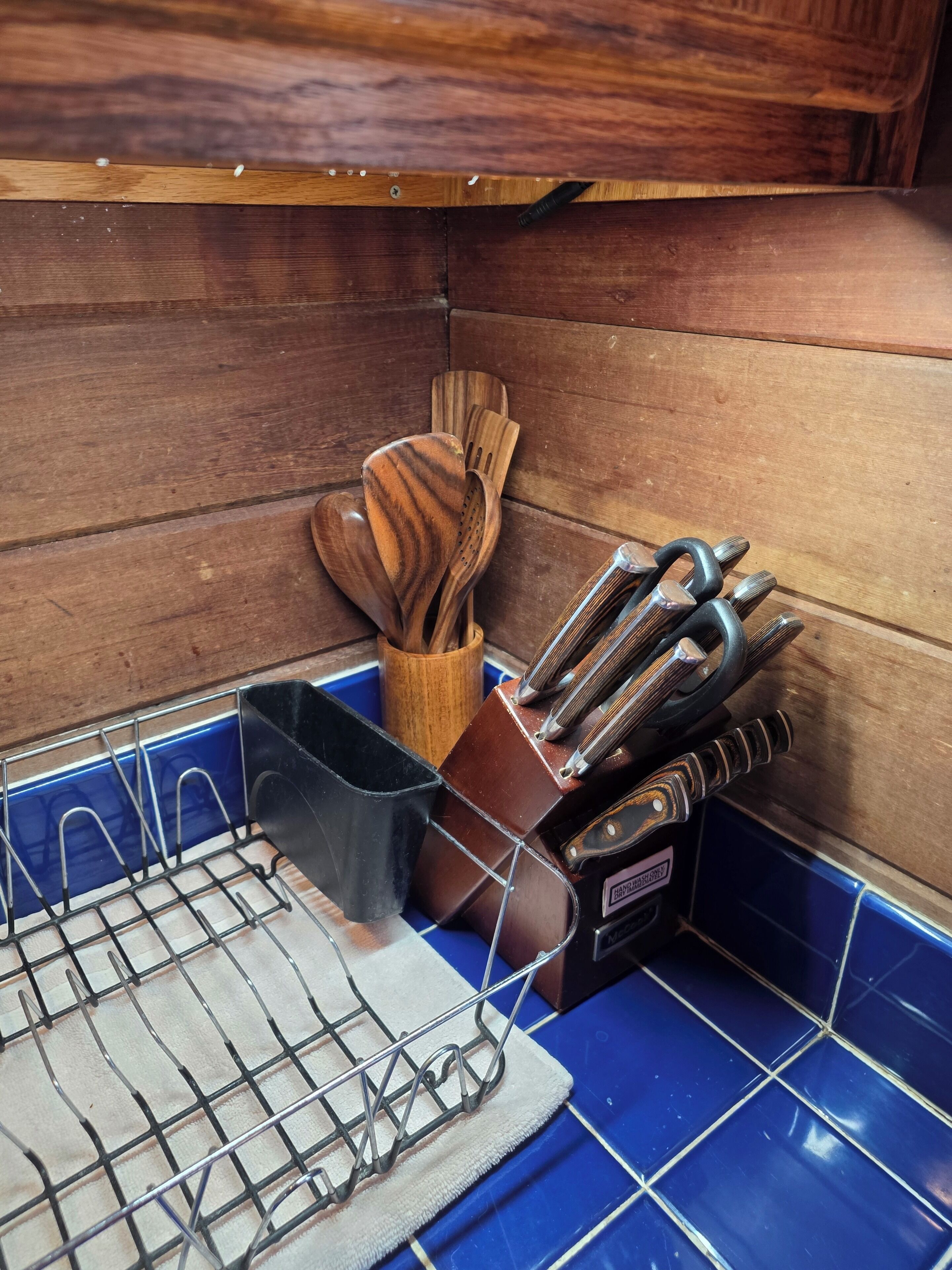 A kitchen area with wooden cabinets, a blue tiled backsplash, and various utensils including a wooden spatula and a knife block.