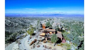A two-story house with a red roof, surrounded by trees and a dirt path, overlooking a valley. - Scenic Getaway - Rustic Cabin - Mountain Ridge (Pinon Hills)