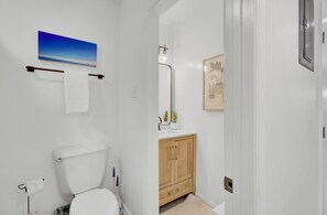 A bathroom with a toilet, a sink with a mirror, a towel rack, and a framed picture on the wall. - Coastal Grove by Avantstay 3 Unit Buyout Minutes From Folly Beach (Folly Beach)