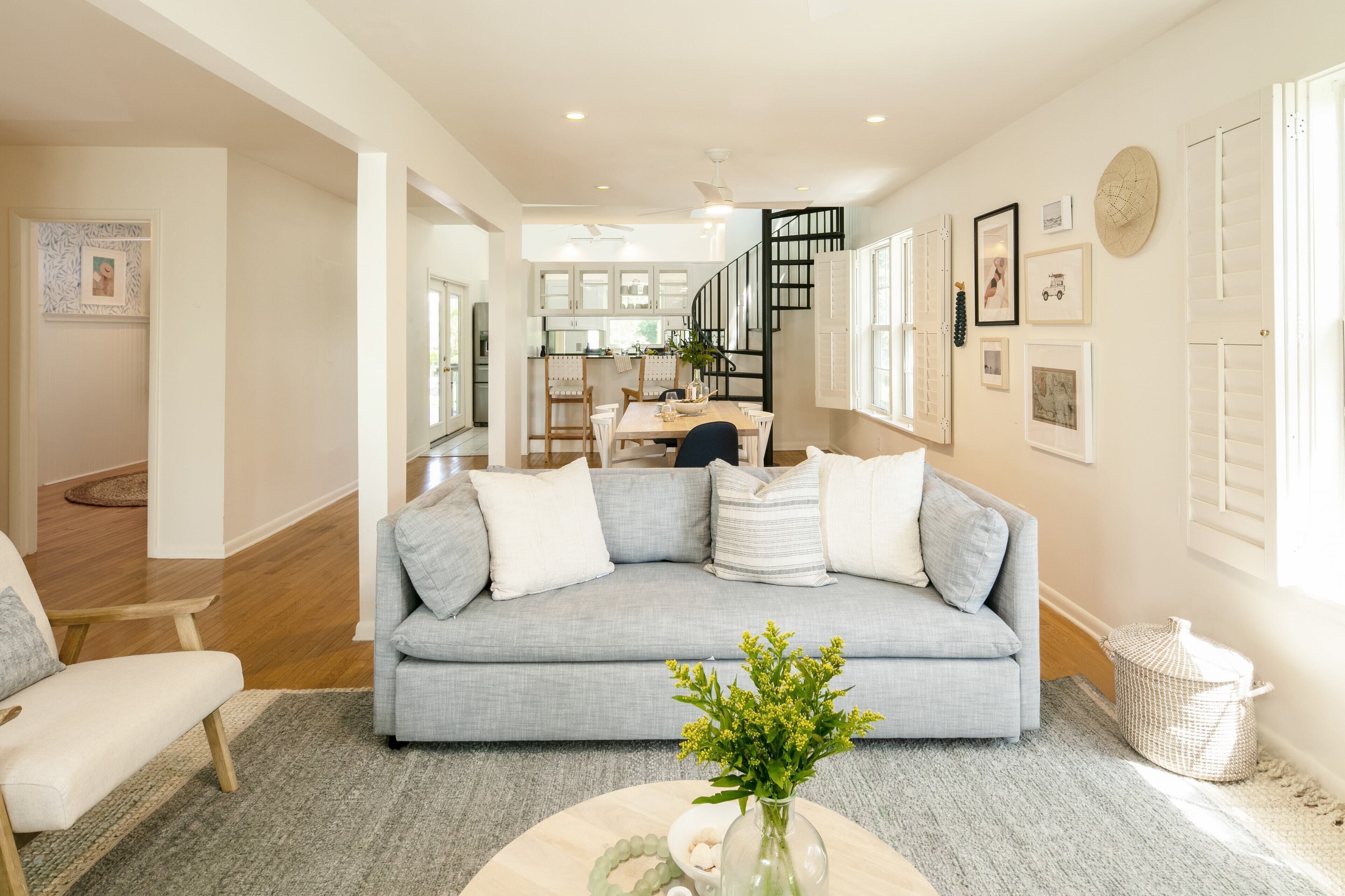 A spacious living room with a grey sofa, a coffee table with a vase, and a dining area in the background.