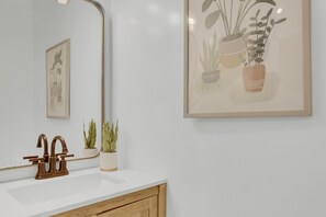 A bathroom with a white sink, a mirror, and two potted plants.