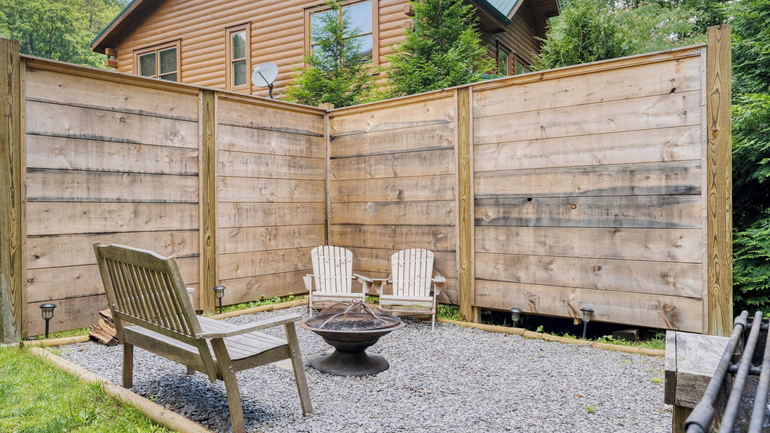 A wooden deck with Adirondack chairs, a fire pit, and a wooden fence.